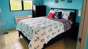 Un dormitorio con cama, ventana, pared decorada y luz en el techo.
