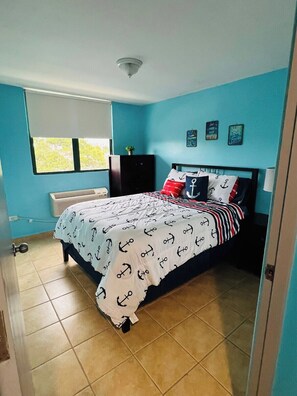 Ein Schlafzimmer mit einem Bett, einem Fenster, einer Wand mit Dekoration und einer Deckenleuchte.
