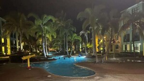 Zona de piscina con palmeras y un edificio al fondo.