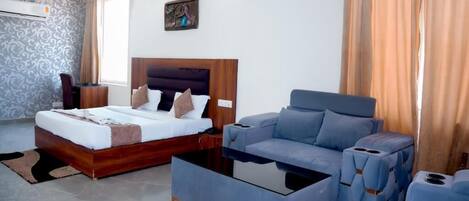A modern hotel room with a bed, a sofa, a coffee table, and a ceiling fan.