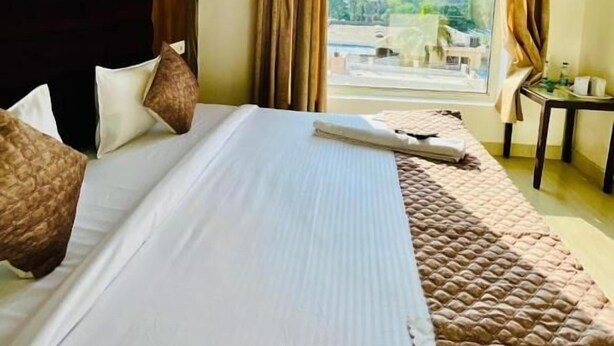 A hotel room with a bed, a view through a window, and a small table with a chair.