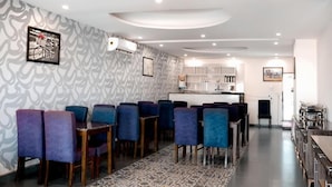 A modern dining area with blue chairs, a patterned wall, and a kitchen in the background.