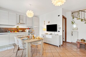 Una cucina moderna con mobili bianchi, un tavolo da pranzo con sedie, un televisore e oggetti decorativi alle pareti.