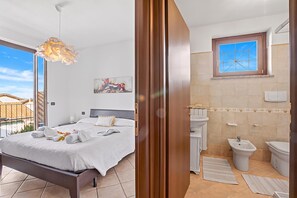 Hotelkamer met bed, nachtkastje, schilderij, raam en badkamer met wastafel, toilet en bidet.
