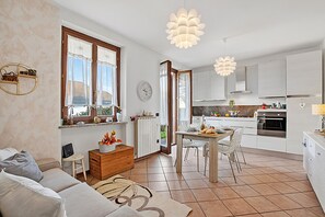 Eine moderne Küche mit weißen Schränken, ein Essbereich mit Tisch und Stühlen sowie ein Wohnzimmer mit Sofa und Couchtisch.