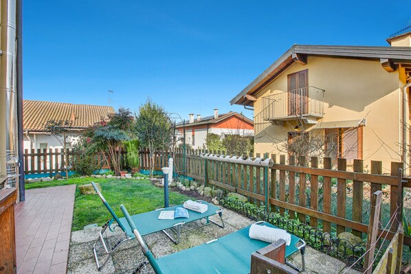 Un giardino sul retro con prato verde, recinzione in legno e un piccolo patio con tavolo e sedie.