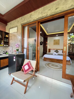 Une chambre moderne comprenant un lit, une porte coulissante à cadre en bois, un coin cuisine et un espace salon avec un fauteuil.