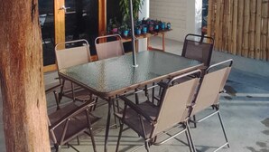 Un patio al aire libre con una mesa y sillas, una planta colgante verde y un cerco de bambú.