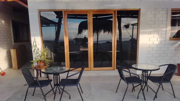 Un patio con dos mesas redondas y cuatro sillas, una planta en maceta y un ventanal corredizo que da a un espacio al aire libre.