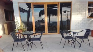 Un espacio al aire libre con dos mesas redondas y cuatro sillas, una planta en maceta y vistas a través de amplios ventanales.