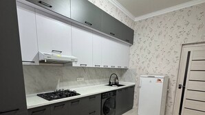 Una cocina compacta con gabinetes grises, encimera blanca, estufa integrada, lavadora y refrigerador.
