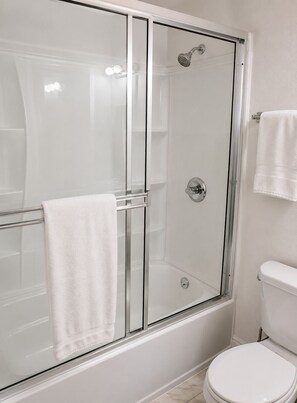Eine gläserne Dusche mit einem weißen Handtuch am Türgriff, eine weiße Toilette und eine weiße Badewanne.