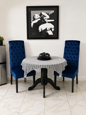 A dining table with a checkered tablecloth, two blue upholstered chairs, and a framed black and white artwork on the wall. - Peaceful Studio • Full Kitchen • Prime Location (Las Vegas)