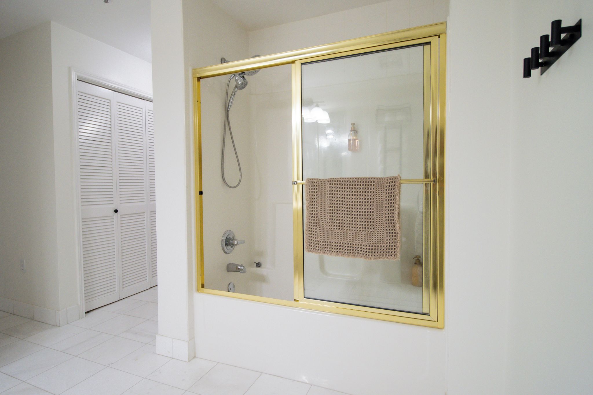A bathroom with a glass shower enclosure, a towel rack, and a white tiled floor.