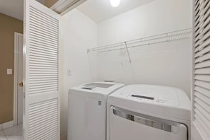 Un cuarto de lavandería con dos secadoras blancas y un estante metálico encima.