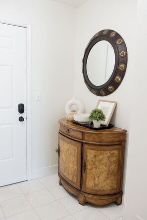 A white door, a wooden cabinet with a mirror, and a small plant on the cabinet.