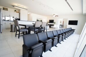 A modern hotel room with a long row of black chairs, a dining area with a white table, and a TV mounted on the wall.