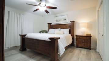 Une chambre à coucher avec un lit en bois, une table de chevet avec une lampe, un ventilateur de plafond et un tableau encadré au mur.