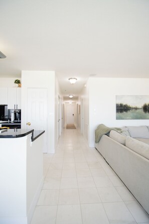 A modern kitchen with white cabinets and a black countertop, leading to a hallway with a white door at the end.
