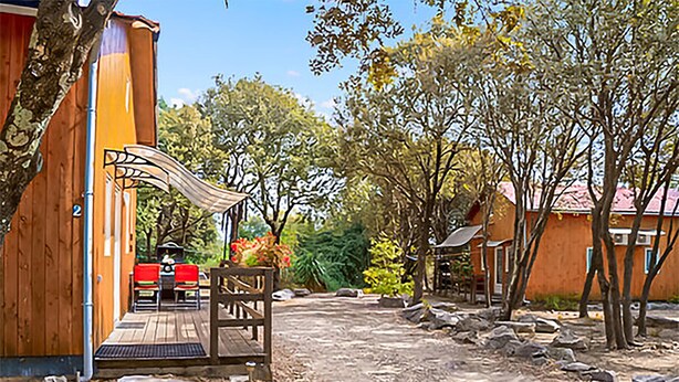 Un bâtiment en bois doté d’un patio couvert, d’un chemin de terre et entouré d’arbres.