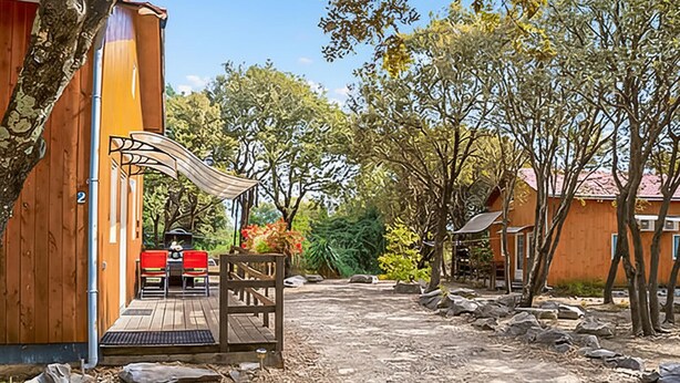 En træbygning med terrasse, udendørs møbler og et overdækket område med bord og stole.