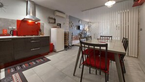 Kompakti keittiö, jossa on punainen työtaso, valkoinen jääkaappi ja ruokailutila, jossa on pöytä ja tuolit.