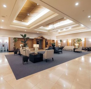 A spacious lobby with a high ceiling, recessed lighting, and a central seating area with sofas and tables.