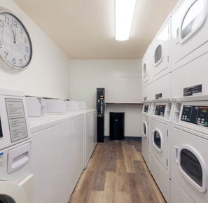 A laundry facility with multiple washing machines and dryers, a clock on the wall, and a control panel.