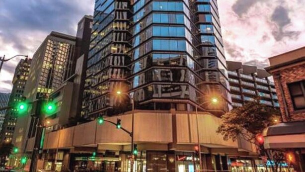 Ein Hochhaus mit moderner Glasfassade, umgeben von anderen Gebäuden und Straßenlaternen.