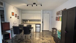 Eine kompakte Küche mit weißen Schränken, eine Essecke mit Tisch und Stühlen, ein Kühlschrank und eine Tür mit Griff.