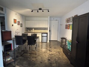 A compact kitchen with white cabinets, a dining area with a table and chairs, a refrigerator, and a door with a handle. - Chic studio condo with Free Parking & AC in vibrant Downtown Honolulu (Honolulu)