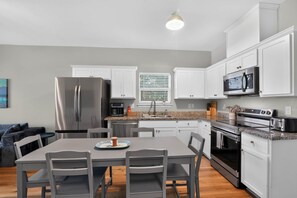 A modern kitchen with white cabinets, stainless steel appliances, and a dining area with grey chairs. - Merchants Quarter 4BR Pet Friendly Beach Gear Propane BBQ (Galveston)