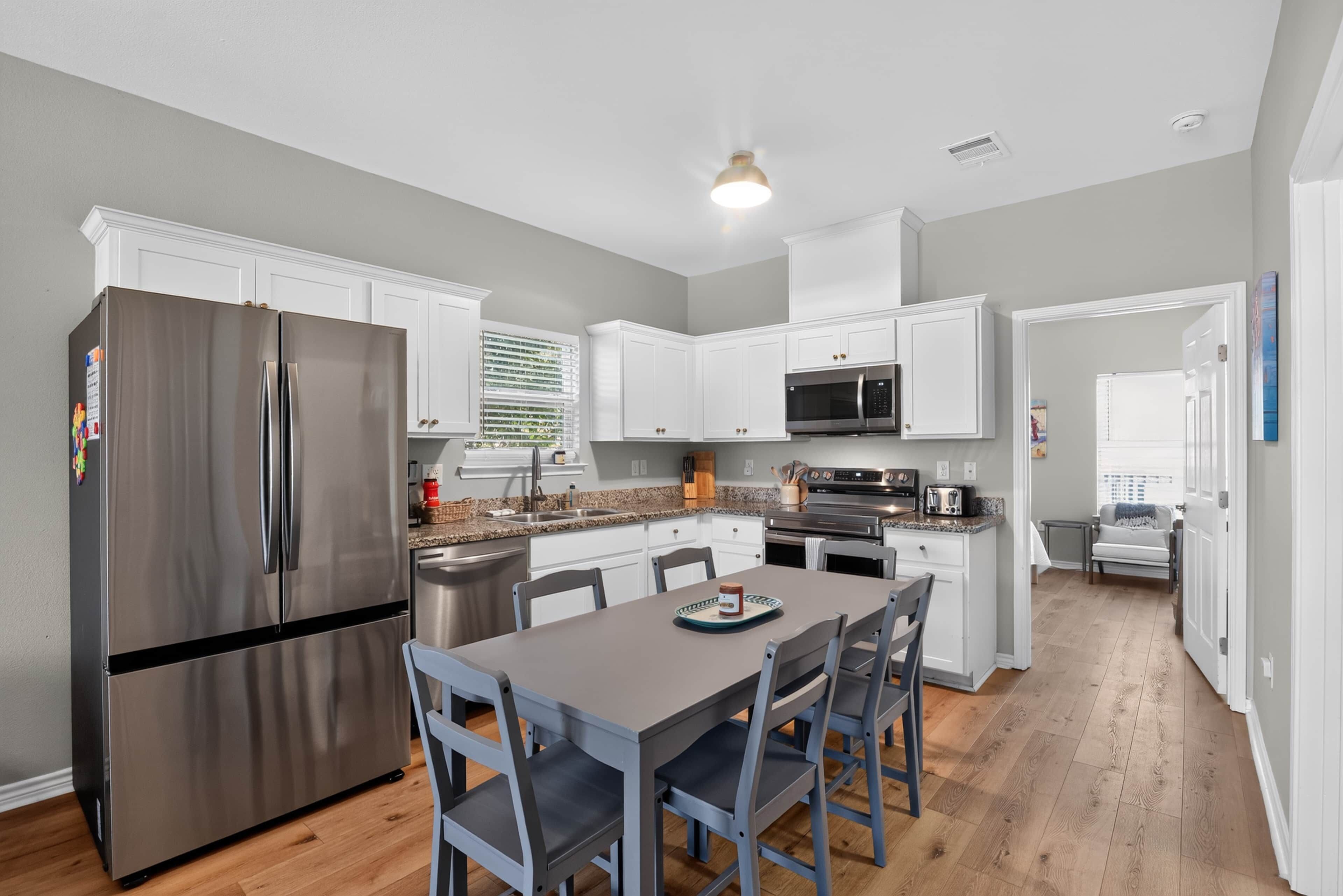 A modern kitchen with white cabinets, stainless steel appliances, and a dining area with a table and chairs.