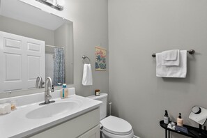 A bathroom with a white sink, a toilet, a towel rack, and a small shelf with toiletries. - Merchants Quarter 4BR Pet Friendly Beach Gear Propane BBQ (Galveston)