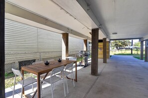 An outdoor covered patio with a wooden table and chairs, a grill, and a chain-link fence. - Merchants Quarter 4BR Pet Friendly Beach Gear Propane BBQ (Galveston)