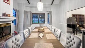 A formal dining room with a long table, chairs, a chandelier, a fireplace, and a piano. - Spacious 4-bedroom house in enchanting Coachella with AC (Coachella)