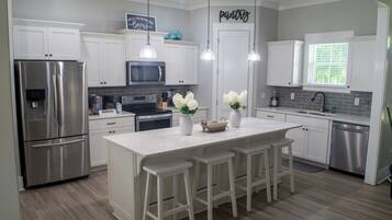 Una cocina moderna con gabinetes blancos, electrodomésticos de acero inoxidable y una isla central con taburetes.