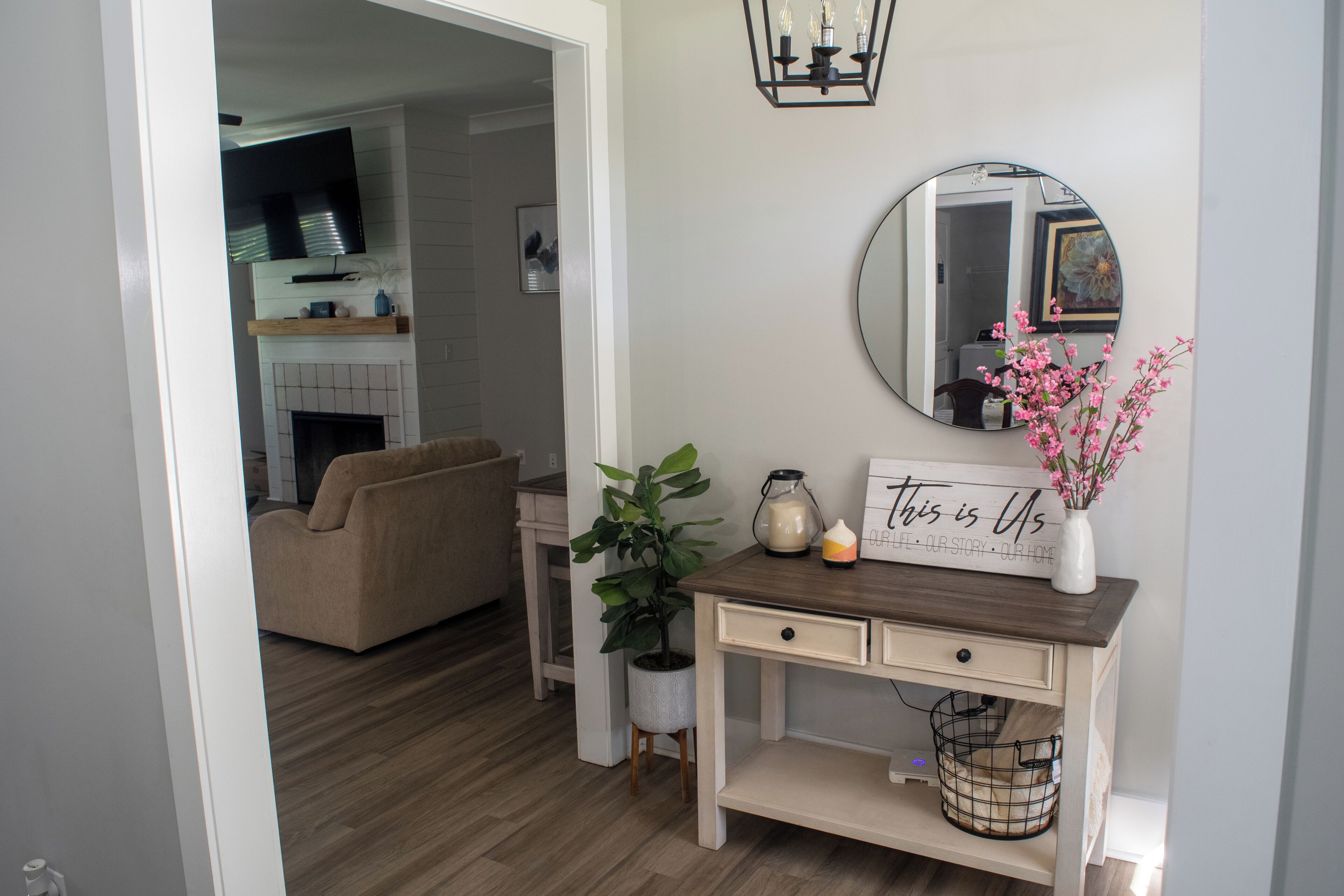 Un salón con sofá, una mesa de centro, una mesita auxiliar con una planta, un espejo y un cartel en la pared.