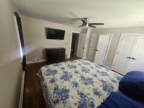 Quarto com uma cama, ventilador de teto, televisão e um conjunto de portas brancas.
