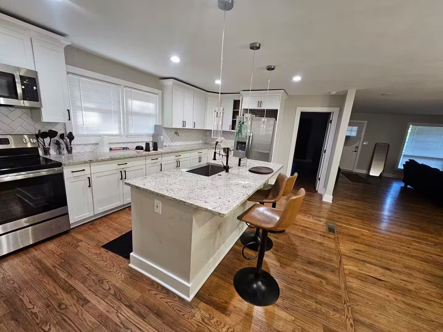 A modern kitchen with white cabinetry, a granite countertop, stainless steel appliances, and a wooden floor.