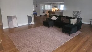 A spacious living area with a large black sectional sofa, a pink rug, and hardwood flooring. - 10 mins from Mercedes Benz stadium! (Atlanta)