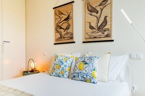 Une chambre à coucher avec un lit, des oreillers, une table de chevet, une lampe et deux illustrations d’oiseaux encadrées accrochées au mur.