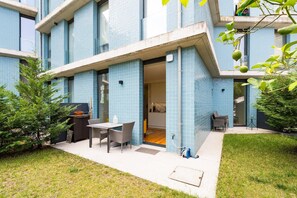 Un bâtiment moderne aux murs extérieurs recouverts de carreaux bleus, doté d’un patio avec des meubles d’extérieur et d’un espace cuisine visible.