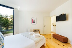 A bedroom with a bed, a bench, a TV, and a door leading to a bathroom. - GuestReady-Modern Retreat with Private Terrace (Porto)