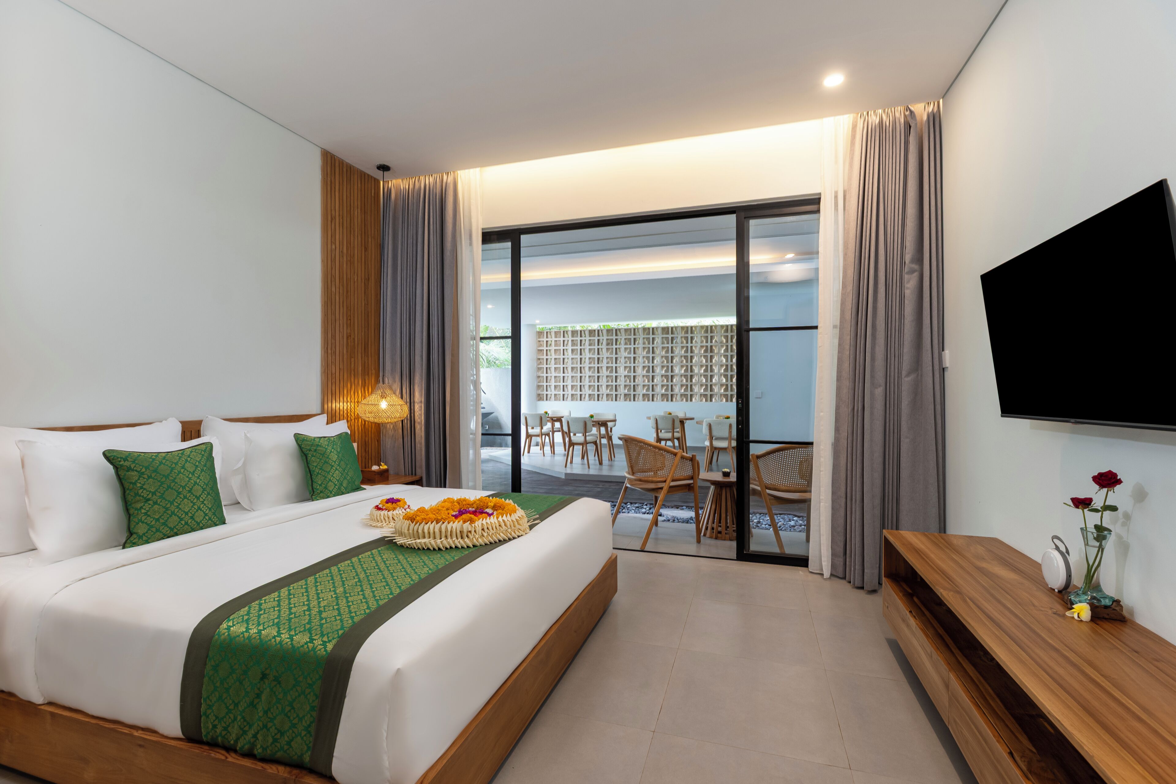 A hotel room with a large bed, a TV, a balcony with chairs, and a dining area.