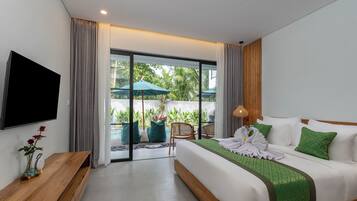 A modern hotel room with a large bed, a flat-screen TV, a wooden bench, and a view of a garden through a glass door.