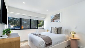 Een moderne slaapkamer met een groot bed, nachtkastjes, een televisie en een raam met uitzicht.