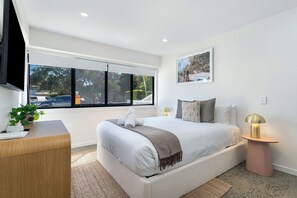 A modern bedroom with a large bed, bedside tables, a TV, and a window with a view of the outside. - Bright Beachside Studio in Miami -1 (Miami)