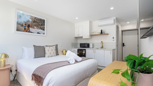 Een hotelkamer met een bed, nachtkastje, een kitchenette en een bloempot.