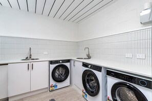 A modern laundry room with two front-loading washing machines, a sink, and a tiled backsplash. - Bright Beachside Studio in Miami -1 (Miami)